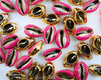 Könnte beinhalten: Eine Sammlung von rosa und goldenen Kaurischnecken. Die Muscheln sind in einem zufälligen Muster auf einer weißen Oberfläche angeordnet.