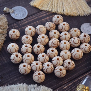 May include: A collection of white beads with brown swirl designs. The beads are arranged on a dark brown wooden surface.