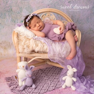 May include: A newborn baby wearing a lavender outfit and floral headband, sleeping peacefully on a small wicker chair. The scene includes a white heart-shaped prop, a knitted purple rug, and stuffed animal toys. The words "sweet dreams photography" are written in cursive.