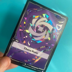 Peut inclure: Une carte violette avec le texte "Chaos Rune" et un motif holographique. La carte a une bordure noire et le mot "RUNE" dans le coin supérieur gauche. La carte est tenue sur un fond bleu.