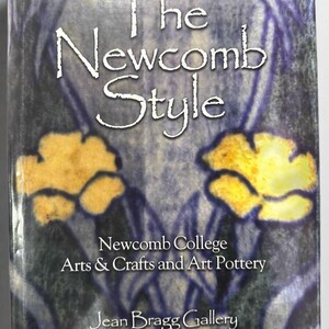 May include: A book titled "The Newcomb Style" with a blue and yellow floral design. The cover also includes the text "Newcomb College Arts & Crafts and Art Pottery" and "Jean Bragg Gallery".