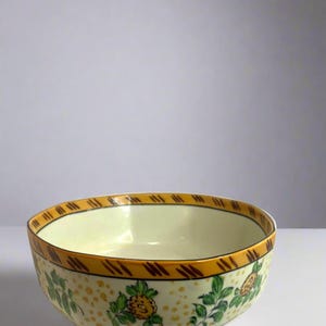 Pode incluir: Uma tigela de cerâmica branca com uma borda listrada amarela e marrom e um padrão floral em verde e amarelo.