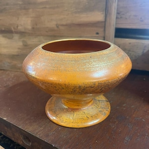 May include: A ceramic planter with a wide, round bowl and a pedestal base. The planter is a warm orange colour with a metallic gold glaze.