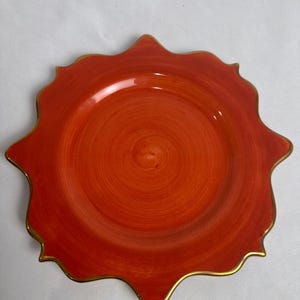 May include: An orange decorative plate with a gold rim. The plate has a unique, scalloped edge and a glossy finish. The centre of the plate has a spiral design.