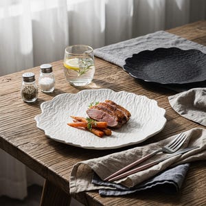 Pode incluir: Uma mesa de jantar com um prato branco texturizado com pato cozido e cenouras. Um prato preto, um copo de água com limão e alecrim, saleiros e pimenteiros e talheres também estão presentes. A mesa é de madeira.