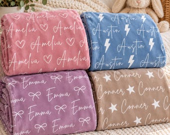 Op de afbeelding: Vier gevouwen pluche dekens in roze, blauw, paars en beige. De roze deken toont de naam Amelia en hartjes. De blauwe deken toont de naam Austin en bliksemschichten. De paarse deken toont de naam Emma en strikjes. De beige deken toont de naam Conner en sterren.