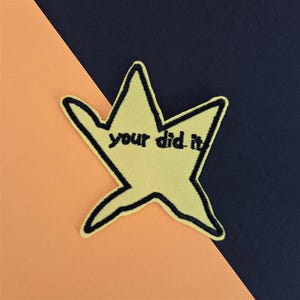 May include: Yellow star-shaped patch with black outline and the embroidered text "your did it". The patch is set against a background of orange and navy blue.
