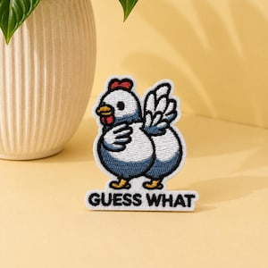 May include: An embroidered patch featuring a cartoon chicken with white and blue feathers, a red comb, and a yellow beak. The chicken is looking over its shoulder with one wing raised. Below the chicken, the text GUESS WHAT is embroidered in black.