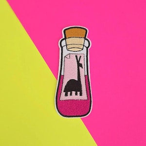 May include: Embroidered patch of a pink potion bottle with a cork stopper and a white label with a black llama illustration. The label reads "Llama Potion".