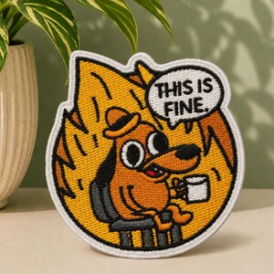 May include: An embroidered patch featuring a cartoon dog wearing a hat, sitting in a chair amidst orange and yellow flames, holding a white mug. A speech bubble above the dog contains the black text THIS IS FINE. The patch has a white border.