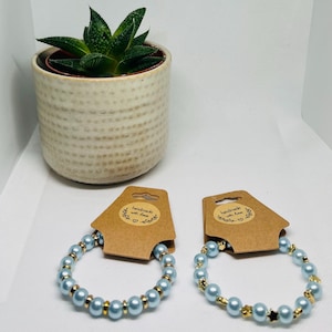 May include: Two beaded bracelets on brown cardboard display cards. One bracelet features light blue round beads with gold-tone spacers. The other features light blue round beads with small gold-tone star-shaped spacers. Each card says handmade with love.