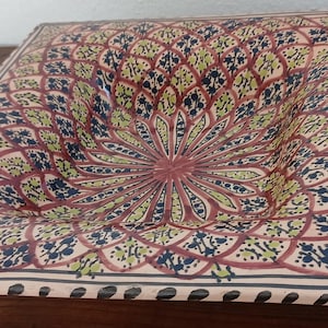 Peut inclure: Plat de service carré en céramique avec un motif floral dans les tons de rouge, vert et bleu marine. Le plat a un centre légèrement concave et une bordure décorative. Le design est symétrique et détaillé.