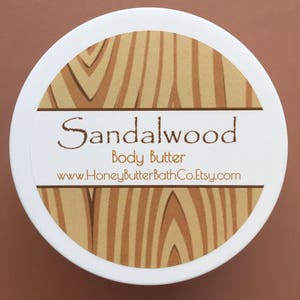 May include: A white jar with a brown woodgrain pattern label. The label reads "Sandalwood Body Butter" and "www.HoneyButterBathCo.Etsy.com".