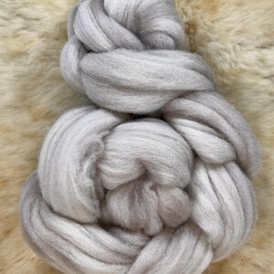 May include: A large bundle of light gray wool roving. The wool is soft and fluffy, and it is perfect for spinning or felting.