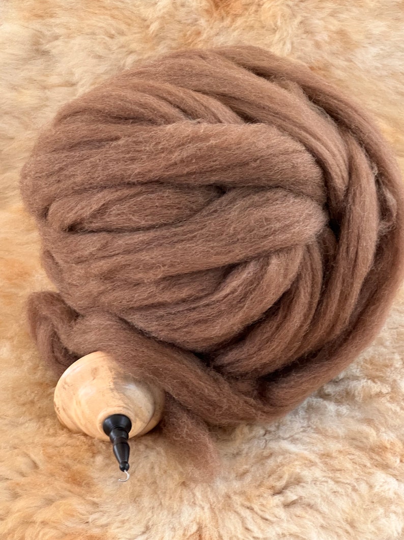 K&ouml;nnte beinhalten: Ein gro&szlig;er Ball brauner Wolle, bereit zum Spinnen. Die Wolle ist weich und flauschig und perfekt zum Herstellen von Garn zum Stricken oder H&auml;keln.