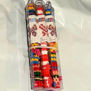 May include: Three clear plastic tubes filled with colorful building blocks. Each tube has a label that reads "Building Blocks".