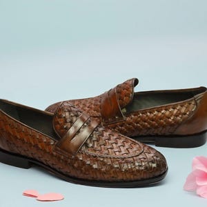 May include: A pair of brown leather woven loafers with a tassel detail. The loafers are on a light blue background with pink flowers.