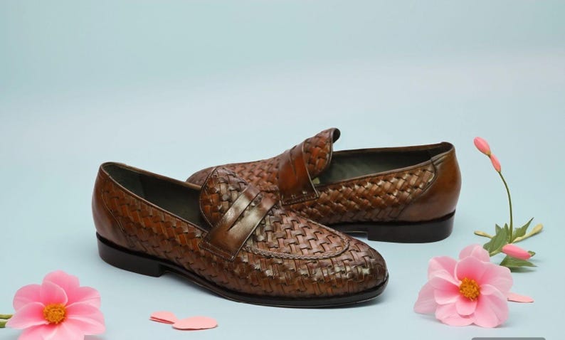 May include: A pair of brown leather woven loafers with a tassel detail. The loafers are on a light blue background with pink flowers.