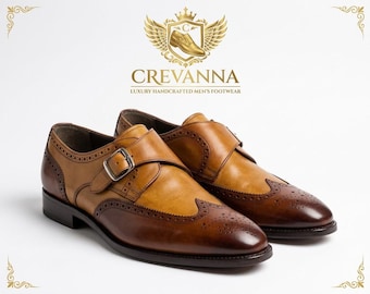 May include: A pair of two-tone tan and dark brown leather monk strap shoes featuring brogue detailing, a silver-tone metal buckle, and a stacked heel. The logo above reads CREVANNA LUXURY HANDCRAFTED MEN'S FOOTWEAR with a winged crest emblem.