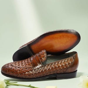 May include: Brown leather woven loafers with a decorative stitch pattern. The loafers have a pointed toe and a leather sole.
