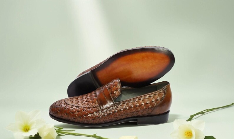 May include: Brown leather woven loafers with a decorative stitch pattern. The loafers have a pointed toe and a leather sole.