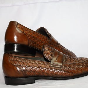 May include: A pair of brown leather loafers with a woven design. The loafers have a black leather sole and a pointed toe.