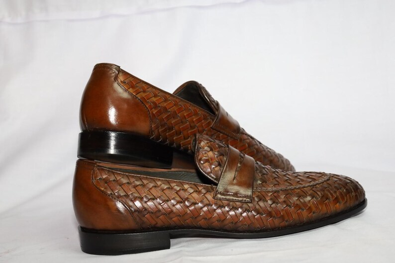 May include: A pair of brown leather loafers with a woven design. The loafers have a black leather sole and a pointed toe.