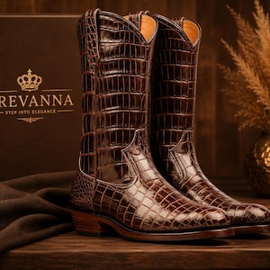 May include: A pair of dark brown cowboy boots featuring a textured crocodile skin pattern. The boots have a pointed toe, a stacked wooden heel, and a tall shaft. Next to the boots is a brown box with the text CREVANNA STEP INTO ELEGANCE.