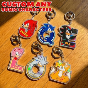 May include: Keychains featuring various Sonic the Hedgehog characters, each with a unique design and name. The keychains are made of clear acrylic and have silver key rings. The text "CUSTOM ANY SONIC CHARACTERS" is at the top.