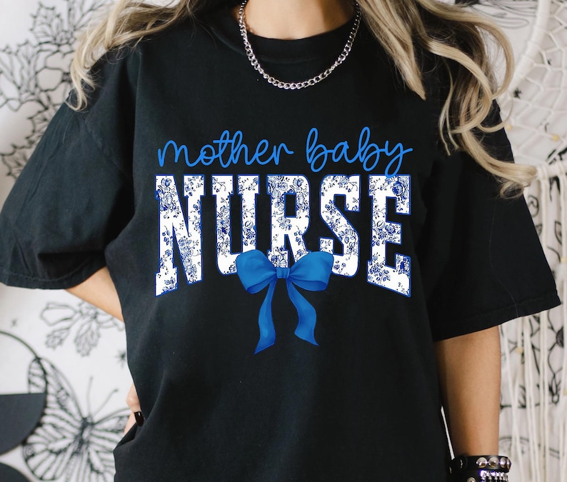以下が含まれることがあります： 白い花柄と青いリボンが付いた黒いTシャツ。Tシャツには「mother baby NURSE」の文字がプリントされています。
