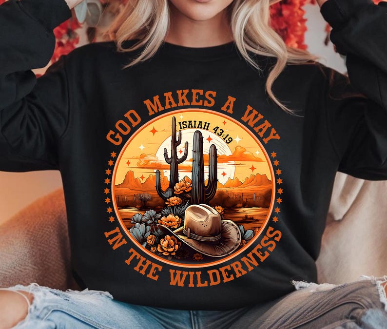Może przedstawiać: Czarna bluza z nadrukiem przedstawiającym scenę z pustyni z kaktusem i kowbojskim kapeluszem. Tekst "God Makes A Way In The Wilderness" jest napisany w k&oacute;łku wok&oacute;ł nadruku. Tekst "Isaiah 43:19" jest r&oacute;wnież zawarty w nadruku.