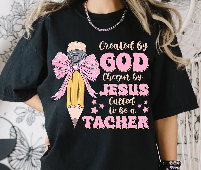 Może przedstawiać: Czarny T-shirt z r&oacute;żowym tekstem, kt&oacute;ry brzmi "Stworzony przez BOGA Wybrany przez JEZUSA Powołany, aby być NAUCZYCIELEM" i r&oacute;żową kokardką z ż&oacute;łtym oł&oacute;wkiem w środku.