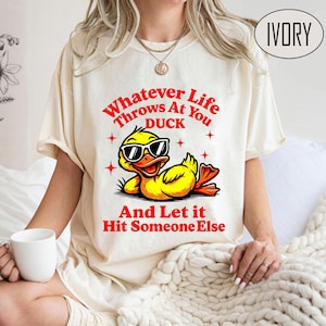 May include: A white t-shirt with the text "Whatever Life Throws At You Duck And Let It Hit Someone Else" in red. A cartoon duck wearing sunglasses is in the center of the shirt.