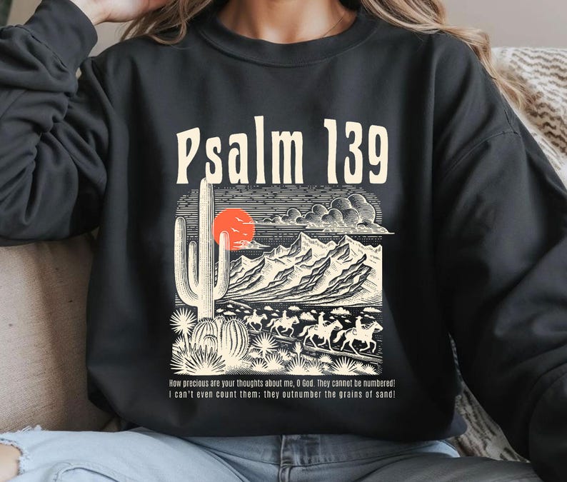 Puede incluir: Sudadera negra con un estampado gr&aacute;fico de un paisaje des&eacute;rtico, un cactus y el texto "Salmo 139". El texto debajo del gr&aacute;fico dice: "&iexcl;Cu&aacute;n preciosos son tus pensamientos acerca de m&iacute;, oh Dios! No se pueden contar. Ni siquiera puedo contarlos: &iexcl;superan en n&uacute;mero los granos de arena!"