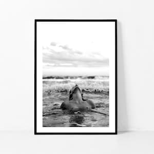 Peut inclure: Une photographie en noir et blanc d'une personne flottant dans l'océan, la tête renversée et les yeux fermés. La personne est entourée de vagues et le ciel est nuageux.