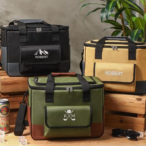 Könnte beinhalten: Drei isolierte Kühltaschen in Schwarz, Beige und Grün, jede mit einer Vordertasche und einem oberen Griff. Die schwarze Tasche hat eine Berg-Grafik und den Namen "ROBERT". Die beige Tasche hat den Namen "ROBERT". Die grüne Tasche hat Golf-Initialen.