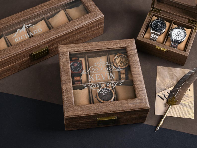 May include: Wooden watch display boxes with glass tops. One box is open, displaying two watches. Another box has the name "RICHARD" etched on the glass. A third box has the name "KEVIN" etched on the glass. The boxes are on a dark surface.