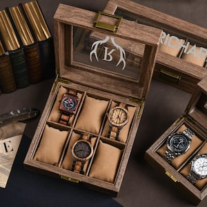 May include: Wooden watch boxes with glass lids, showcasing various wooden and metal watches. One box has a deer antler and letter "K" design, another has the name "RICHARD". The watches have brown, black, and silver tones. The boxes are open, revealing the watches.