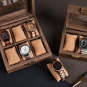 May include: Wooden watch display cases with glass tops, showcasing various wristwatches. The watches feature wooden and metal bands, with different face designs. The cases are open, revealing the watches on tan cushions.