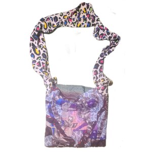 Puede incluir: Un bolso de hombro patchwork con una correa con estampado de leopardo colorido. El cuerpo del bolso presenta un collage de patrones abstractos en tonos de azul, morado y gris. La correa es blanca con manchas amarillas, rosas, azules y negras.