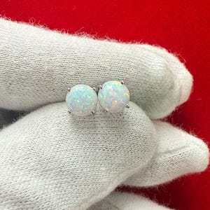 May include: A pair of silver stud earrings featuring white opal stones. The earrings are round and have a smooth, polished finish.
