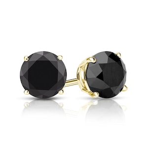 May include: A pair of black diamond stud earrings. The round-cut black gemstones are set in a gold-colored prong setting. The earrings are displayed on a white surface with a slight reflection.