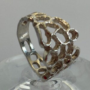 May include: A silver ring featuring a delicate, intricate design. The ring is crafted from a thin band of silver with a pattern of small, interconnected circles and loops. The ring is a unique and stylish piece of jewellery.