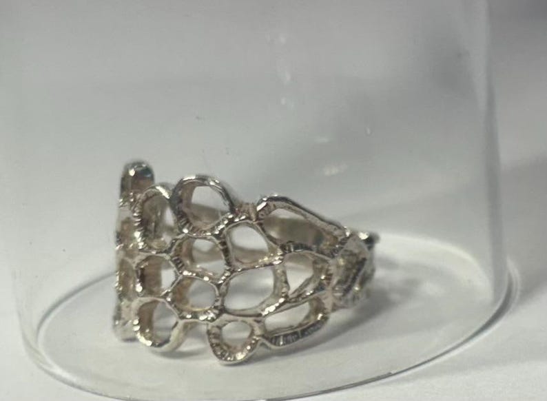 May include: A silver ring with a delicate, openwork design resembling a honeycomb pattern.