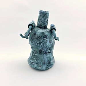 May include: A handmade, blue ceramic vase with a textured surface and two loop handles. The vase has a cylindrical neck and a bulbous body. The surface is covered in a crosshatch pattern.