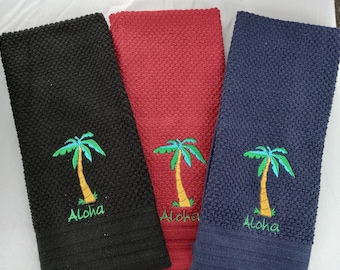 May include: Three kitchen towels with a palm tree and "Aloha" embroidered on them. The towels are black, red, and navy blue.