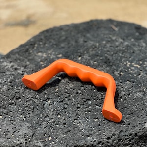 May include: Orange plastic handle with a textured grip. The handle is designed for lifting or carrying heavy objects.