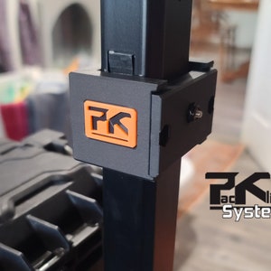 Puede incluir: Primer plano de un soporte met&aacute;lico negro con un logotipo naranja y negro. El logotipo presenta las letras "PK" dentro de un cuadrado. Las palabras "PK Faclip System" est&aacute;n impresas en blanco debajo.