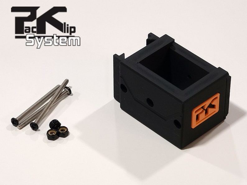 Puede incluir: Un componente de pl&aacute;stico negro con un logotipo naranja, acompa&ntilde;ado de tornillos plateados y tuercas negras. El componente tiene forma rectangular con un interior abierto. El texto "PK Clip System" es visible.