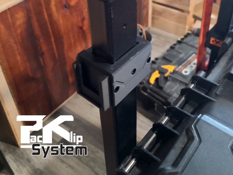 Puede incluir: Sistema de clip Pack negro con el texto "PK Pack Clip System" en blanco. El sistema est&aacute; fijado a un poste de metal negro. Un clip de pl&aacute;stico negro est&aacute; fijado al poste. El fondo incluye una superficie de madera y una caja de herramientas negra.